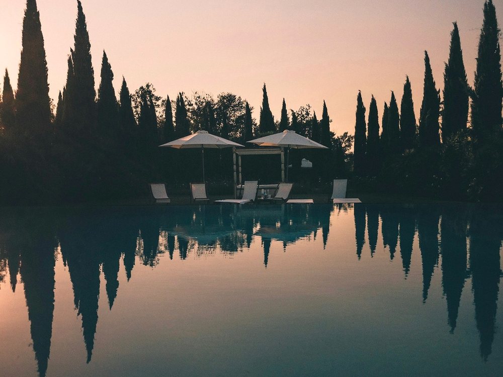 Hotelaria: piscina de hotel ao entardecer, entre ciprestes